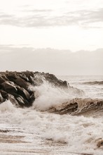 Vertical Shot Of Waves Splashing Onto The Rocky Shore During Daytime