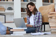 © ty - Smiling young female sitting on the floor in the living room student studying at home working with her laptop.