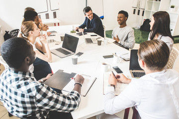 A team of young office workers, businessmen with laptop working at the table, communicating together in an office. Corporate businessteam and manager in a meeting. coworking.