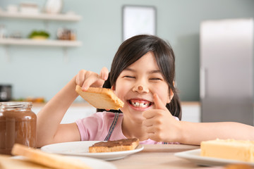 Canvas Print - Funny little girl eating tasty toasts with chocolate spreading in kitchen