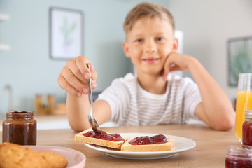 Canvas Print - Funny little boy eating tasty toasts with jam in kitchen