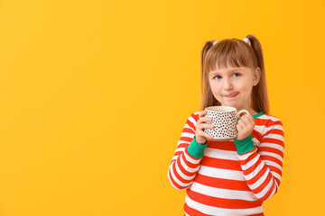 Wall Mural - Cute little girl drinking hot chocolate on color background