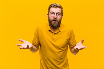 Wall Mural - young blonde man feeling extremely shocked and surprised, anxious and panicking, with a stressed and horrified look against orange wall