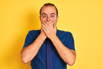 Sticker - Young businessman wearing denim casual shirt and tie over isolated yellow background shocked covering mouth with hands for mistake. Secret concept.