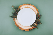 Festive Christmas Natural Style Table Setting With White Plate On Wood Cut Platters And Fir Tree Branches On Green Blue Background. Flat Lay, Top View, Copy Space