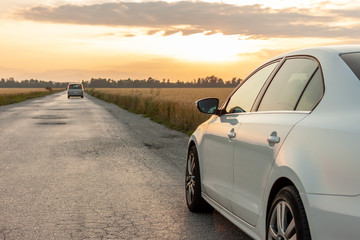 white car on country road next to yellow wheat field