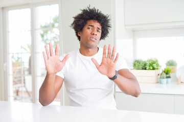 Canvas Print - Young african american man wearing casual white t-shirt sitting at home Moving away hands palms showing refusal and denial with afraid and disgusting expression. Stop and forbidden.