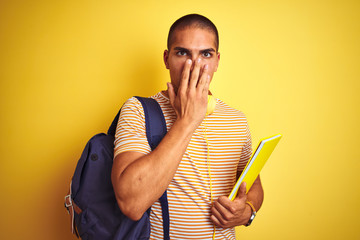 Poster - Young student man wearing headphones and backpack over yellow isolated background cover mouth with hand shocked with shame for mistake, expression of fear, scared in silence, secret concept