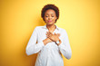 African american business woman over isolated yellow background smiling with hands on chest with closed eyes and grateful gesture on face. Health concept.