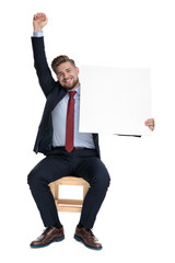 Poster - happy businessman sitting and celebrating success while holding blnk board