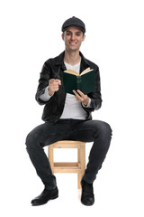 seated casual man holding book while pointing forward confident