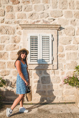 Wall Mural - woman posing in front of stone wall with wooden window with shutter