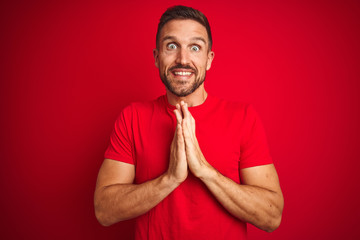 Wall Mural - Young handsome man wearing casual t-shirt over red isolated background praying with hands together asking for forgiveness smiling confident.