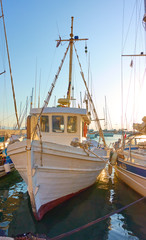 Wall Mural - Old white fishing boat in the port of Aegina at sunset