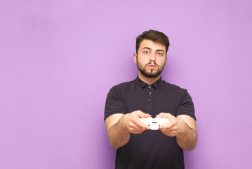 A calm man with a beard with a gamepad in his hands stands on a pink background and looks into the camera. Adult gamer isolated on pink background holding gamepad in hands.