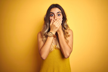 Canvas Print - Young beautiful woman wearing t-shirt over yellow isolated background shocked covering mouth with hands for mistake. Secret concept.