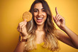 Young beautiful woman eating biscuit over grey isolated background surprised with an idea or question pointing finger with happy face, number one