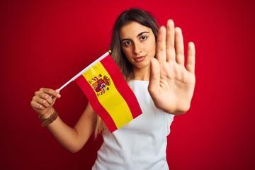 Poster - Young beautiful woman holding spanish flag over red isolated background with open hand doing stop sign with serious and confident expression, defense gesture