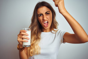 Poster - Young beautiful woman drinking a glass of milk over white isolated background annoyed and frustrated shouting with anger, crazy and yelling with raised hand, anger concept