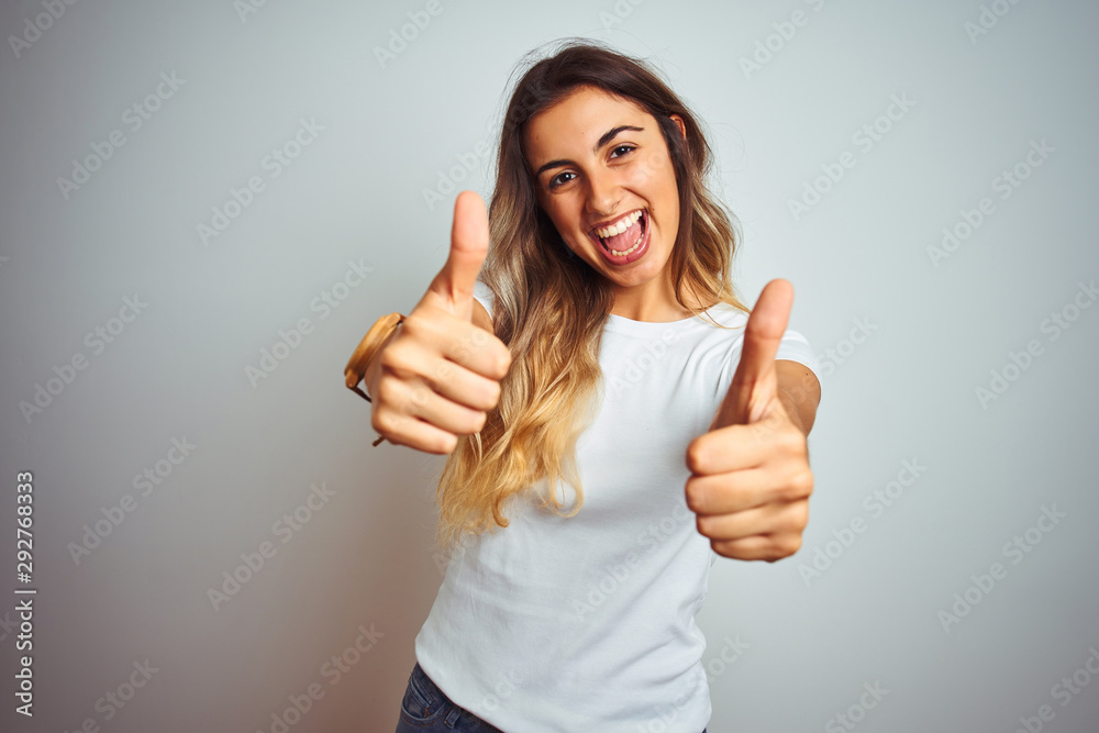 Young beautiful woman wearing casual white t-shirt over isolated background approving doing positive gesture with hand, thumbs up smiling and happy for success. Winner gesture. - obrazy, fototapety, plakaty 