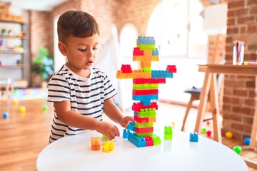 Beautiful toddler boy playing with construction blocks at kindergarten