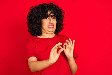 Sticker - Young arab woman with curly hair wearing casual t-shirt over isolated red background disgusted expression, displeased and fearful doing disgust face because aversion reaction. With hands raised