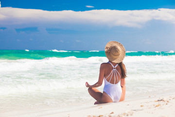 Young woman in bikini and straw hat relaxing at white caribbean beach