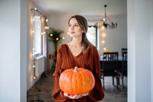 Girl With A Pumpkin Is Standing Near The Table At Home, On The Eve Of The Autumn Holiday