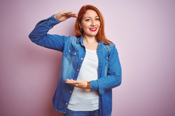 Sticker - Youg beautiful redhead woman wearing denim shirt standing over isolated pink background gesturing with hands showing big and large size sign, measure symbol. Smiling looking at the camera