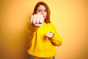 Sticker - Beautiful redhead woman wearing winter sweater standing over isolated yellow background Punching fist to fight, aggressive and angry attack, threat and violence