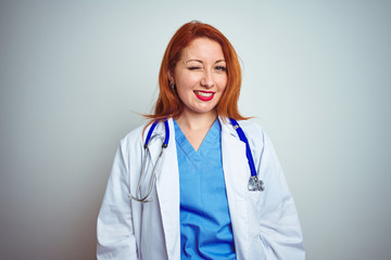 Sticker - Young redhead doctor woman using stethoscope over white isolated background winking looking at the camera with sexy expression, cheerful and happy face.