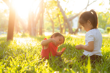 Beautiful young asian kid sitting playing in summer in the park with enjoy and cheerful on green grass, children activity with relax and happiness together on meadow, family and holiday concept.