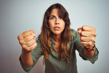 Wall Mural - Young beautiful woman wearing green shirt standing over grey isolated background angry and mad raising fists frustrated and furious while shouting with anger. Rage and aggressive concept.