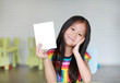 © zilvergolf - Cute little smiling Asian child girl holding blank white paper card in her hand. Kid showing empty paper note copy space in children room.