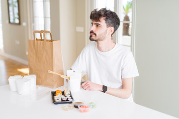 Sticker - Young man eating asian sushi from home delivery looking to side, relax profile pose with natural face with confident smile.