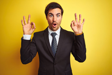 Sticker - Young handsome businessman wearing suit and tie standing over isolated yellow background looking surprised and shocked doing ok approval symbol with fingers. Crazy expression