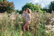 Happy young beautiful woman in sweater and underpants walking with bare foot in a field of dry agrimony