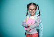 © DN6 - Beautiful smiling Asian little girl with glasses and hold a books with school bag is back to school, empty space in studio shot isolated on colorful blue background, Educational concept for school