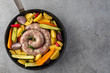 Raw sausages with potatoes, zucchini, carrots and thyme in a grill pan.