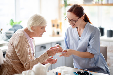 Caregiver wearing glasses giving vitamins to aged lady