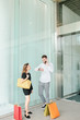 © DragonImages - Young couple standing outside shopping mall, making phone call and looking at watch on his hand