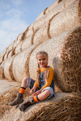 Cute girl having fun on rolls of hay bales in field