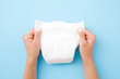 Woman hands holding white baby diaper on pastel blue background. Closeup.