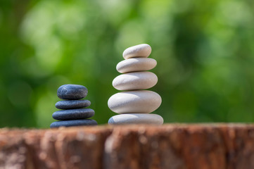 White black stone cairns, poise light pebbles on wood stump in front of green natural background, zen like, harmony and balance