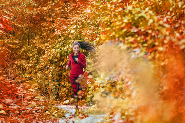 Autumn fall foliage runner woman running in forest woods with beautiful colors in tree leaves nature background. Trail run athlete Asian girl happy training outdoors.