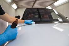 The Process Of Applying A Nano-ceramic Coating On The White Car's Hood By A Male Worker In Blue Gloves With A Sponge And Chemical Composition To Protect The Paint In Detailing Workshop. Auto Service.