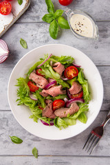 Wall Mural - Salad with roast beef, tomato, onion, lettuce and mustard sauce on light background. Delicious healthy lunch with meat, diet food