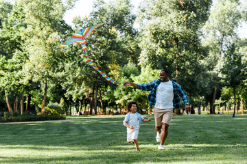 happy african american kid running with father and kite in park