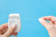 Woman fingers holding new white plastic container with dental floss on pastel blue background. Teeth hygiene concept. Closeup. Point of view shot.