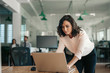 © mavoimages - Businesswoman leaning over her office desk working on a laptop